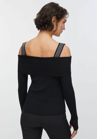 Črna rebrasta majica brez ramen z dolgimi rokavi, iz teksturirane tkanine z okrasnimi naramnicami s kovinskimi zakovicami. Prilegajoč se kroj z minimalnimi detajli.