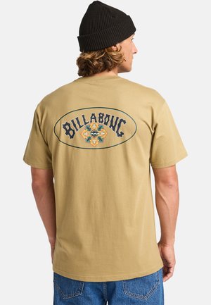 Beige katoenen t-shirt met een groot gedrukt logo in zwart en geel op de rug, met een ronde omtrek en decoratieve elementen.