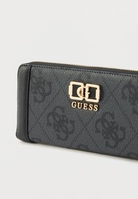 Fekete, texturált pénztárca aranyszínű kapoccsal, amelyen a "GUESS" felirat látható, az anyagon pedig finom logóminta található. Cipzáras záródás.