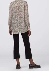 Blusa chiara con motivo a foglie, maniche lunghe e piega sul retro, abbinata a pantaloni neri a 3/4 e mocassini neri con suola spessa.