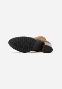 Stivale alla caviglia in suede marrone con suola in gomma nera caratterizzata da un motivo testurizzato e un tacco basso impilato.