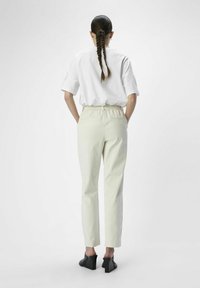 Camiseta blanca oversize y pantalones beige claros ajustados con cintura elástica, combinados con mules de tacón bloque negro, vistos desde atrás.
