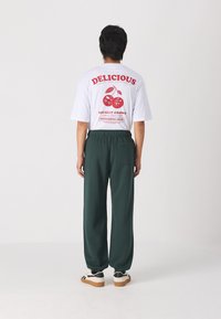 White T-shirt with red graphics featuring cherries, paired with dark green sweatpants. Footwear is white with black accents and a gum sole.