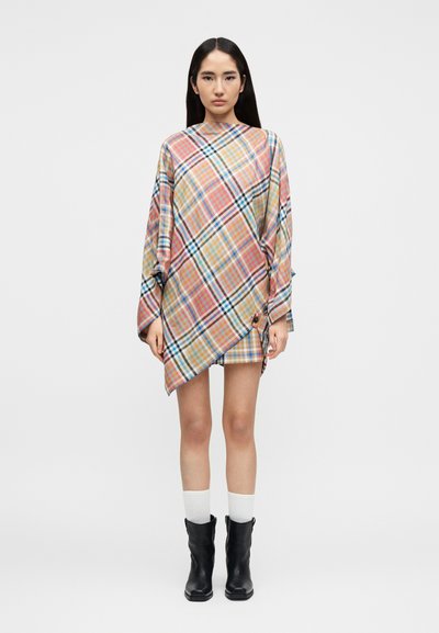 Robe à carreaux avec un ourlet asymétrique, dans des couleurs pastel comme le rose, le bleu et le jaune. Manches longues et coupe ample. Portée avec des bottes noires.