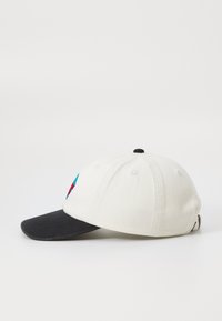 Baseballcap med en hvid stofkrop, sort skygge og farverig broderet design foran. Justerbar strop bagpå for størrelse.