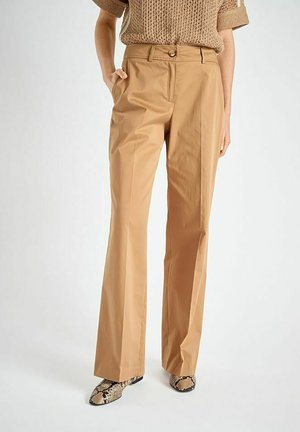 Pantalon large couleur sable en tissu lisse. Il présente une fermeture à boutons à l'avant, des passants pour ceinture et des poches latérales. Associé à des chaussures à motifs.