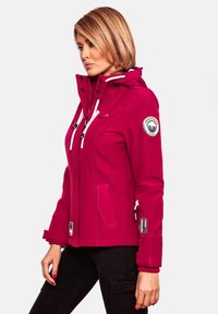 Fuchsia softshell jacket with a detachable hood, white drawstrings, side pockets, and a circular logo patch on the sleeve.