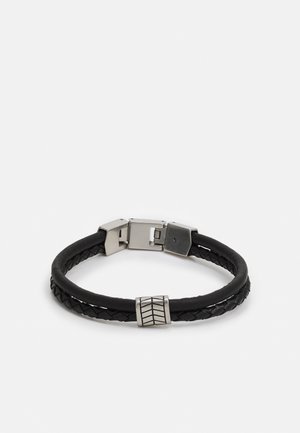 Bracelet en cuir noir double tressé avec fermoir en argent et un accent argenté cylindrique à motifs sur fond blanc.