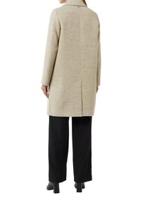 Beige visgraatjas met een gestructureerde kraag, sluiting met één knop en lange mouwen. Gekocht boven zwarte wijde broek en laarzen met hak.
