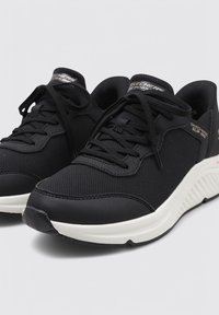 Schwarze Sportschuhe aus Netz- und Synthetikmaterialien, mit einer weißen Sohle, runder Zehenform und Schnürdesign.