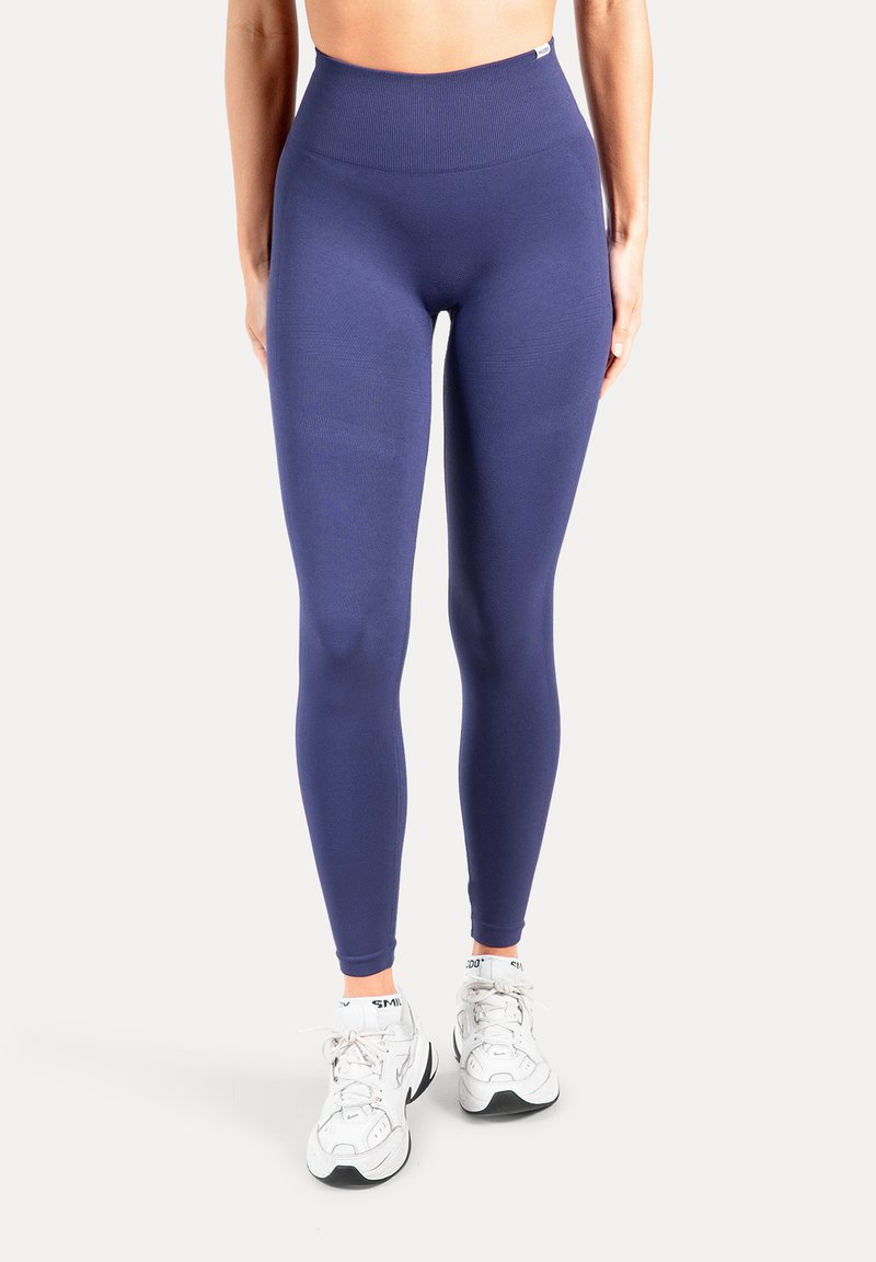 Leggings taille haute bleu marine avec une texture lisse et une coupe ajustée, associés à des chaussures de sport blanches et des chaussettes avec des accents orange.