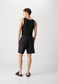 Débardeur noir et shorts en tissu léger, avec une taille élastique et des poches, portés avec des sandales sombres.