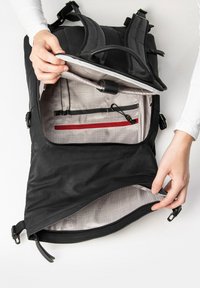 Schwarzer Rucksack mit strukturiertem Außenmaterial, Innentaschen mit kariertem Futter, roter Reißverschlusstasche und verstellbaren Riemen.