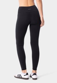 Černé legíny s vysokým pasem, vyrobené z elastické tkaniny, hladkého povrchu a bez viditelných vzorů. Nosit se bílými teniskami.