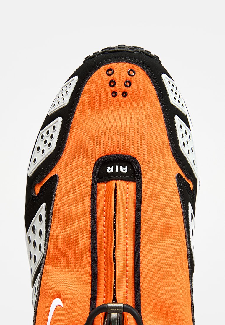 Calzado Nike con parte superior de tejido naranja, acentos negros y detalles en blanco. Incluye detalles perforados y un zip central.