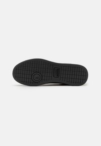 Suola di scarpa in gomma nera con un motivo testurizzato per la presa, caratterizzata da un logo circolare accentuato al centro e un design piatto per la stabilità.