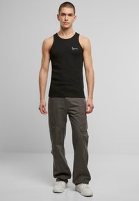 Schwarzes Baumwoll-Top mit geripptem Stoff, versehen mit einem kleinen weißen Logo. Kombiniert mit grauen Cargo-Hosen und weißen Sneakers.
