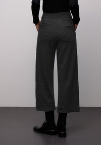 Pantalon large gris foncé texturé avec taille haute et poches arrière, associé à des bottines noires.