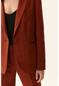 Rostfärgad linneblazer med slagkrage, enkel knappstängning och subtilt texturerad tyg, i kombination med matchande byxor.