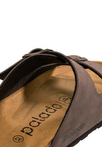 Sandalo in suede marrone con una soletta texture, due cinghie incrociate e un accento di fibbia metallica. Contrassegnato con "palado" e prodotto in Spagna.