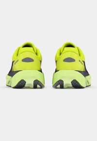 Αθλητικά παπούτσια σε νεον κίτρινο χρώμα με σκούρες λεπτομέρειες, υφή στην επάνω επιφάνεια και παχιά, μαξιλαρωμένη σόλα. Πίσω όψη που δείχνει το σχεδιασμό της φτέρνας και το μοτίβο της σόλας.