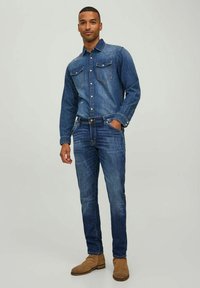Conjunto de camisa de denim y jeans en azul oscuro. La camisa presenta dos bolsillos en el pecho y botones de presión; los jeans tienen un corte ajustado. Combinados con botas beige.