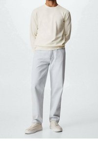 Suéter de manga larga color beige claro con puños y dobladillo acanalados, combinado con jeans rectos color gris claro y zapatillas color crema. Diseño simple, textura suave.