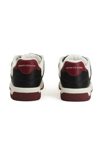 Un paio di sneaker Armani Exchange nere, bianche e borgogna viste da dietro con il nome del marchio sui talloni borgogna.