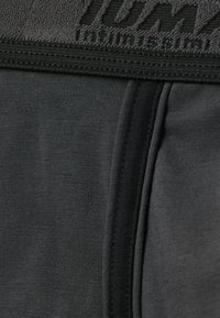 Czarna tkanina odzieżowa z bliska, z teksturowanym pasem z wypukłym napisem, gładkim materiałem bazowym i subtelnym połyskiem w ciemnych odcieniach.