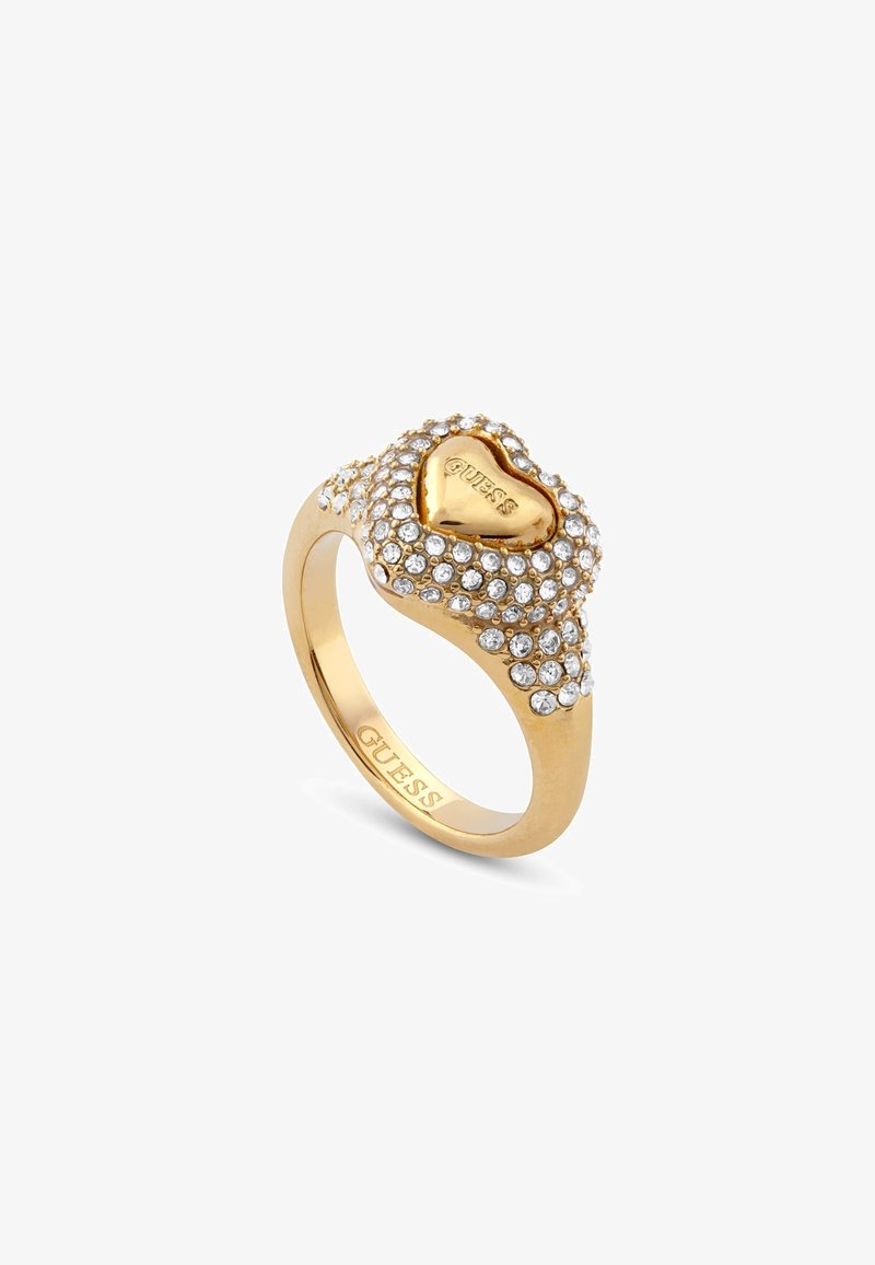 Bague en cœur dorée ornée de cristaux transparents. L'anneau porte la mention 'GUESS' gravée à l'intérieur. La forme en cœur au sommet a une finition lisse.