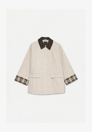 Bézs kabát sötétbarna kordbársony gallérral és kockás mandzsettalábbal, elülső fedeles zsebekkel és hosszú ujjakkal.