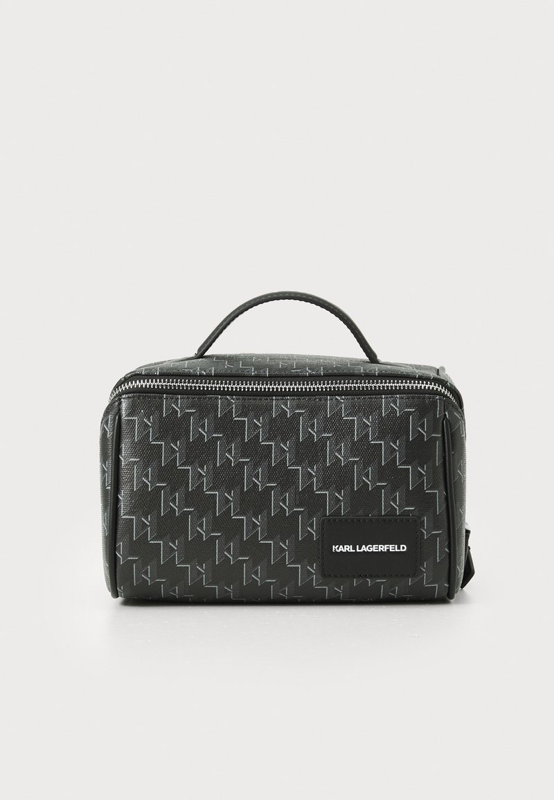 Black cosmetic case with textured exterior, featuring a geometric pattern, top handle, and zip closure. Includes logo patch on the front.