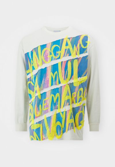 Ilgų rankovių marškiniai šviesiai kreminės spalvos, su ryškiu, spalvingu grafiku ir geltonais bei mėlynais užrašais priekyje, švelni medvilnės tekstūra.