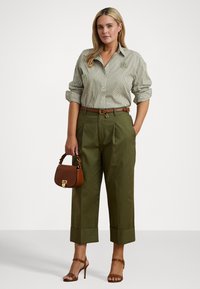 Prúžkovaná košeľa na gombíky, olivové nohavice s vysokým pásom, hnedý opasok a malá hnedá kabelka. Outfit dopĺňajú lodičky na tenkom podpätku.