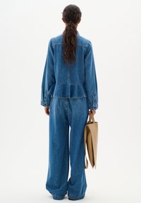 Denim takki, jossa on peplum-muotoilu ja pitkät hihat, yhdistettynä leveälahkeisiin farkkuihin. Kuvassa näkyy myös sininen denim-kangas ja vaalea käsilaukku.