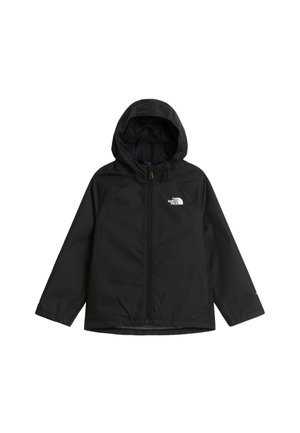 Garçon portant une veste noire North Face et un pantalon de survêtement gris, debout avec les mains dans les poches de la veste, souriant à la caméra.