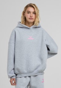 Valkoinen harmaa huppari, joka on valmistettu puuvillasekoitteesta ja jossa on vaaleanpunainen brodeerattu "felicious"-logo rinnassa. Huppari on löysähkössä istuvuudessa ja siinä on ribbaushelma.