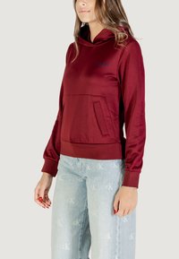 Felpa borgogna con tasca a marsupio, polsini a coste e orlo arrotondato. Tessuto morbido con una leggera lucentezza e dettaglio del logo ricamato.