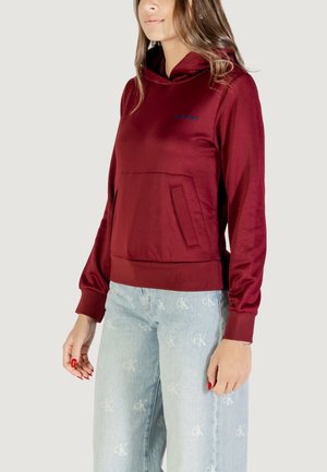 Sudadera burdeos con un bolsillo tipo canguro, puños acanalados y dobladillo redondeado. Tejido suave con un sutil brillo y detalle de logo bordado.