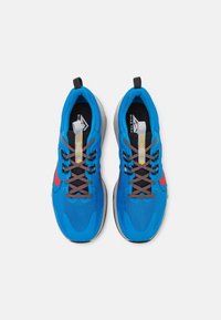 Chaussures de sport bleues avec une tige en maille, des accents gris, des lacets noirs et un logo rouge. Elles présentent un col rembourré et une semelle texturée.