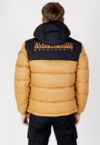 Giacca a vento con cappuccio nero e parte superiore nera, parte inferiore marrone dorato, con un grande logo sul retro e una texture trapuntata.