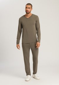 Grå långärmad V-ringad topp i kombination med matchande byxor. Mjukt, elastiskt tyg med en slät yta. Modell som bär vita sneakers.