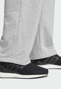 Čierne športové topánky s jemnou sieťovinou a bielou medzipodrážkou; skombinované s voľnými šedými teplákmi s mäkkou textúrou a rovnými nohavicami.