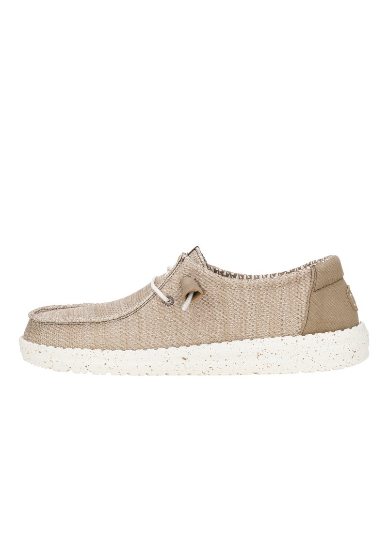 Zapato textil beige con parte superior texturizada, presenta una suela blanca con manchas, puntera redonda y cordones ajustables para un ajuste seguro.