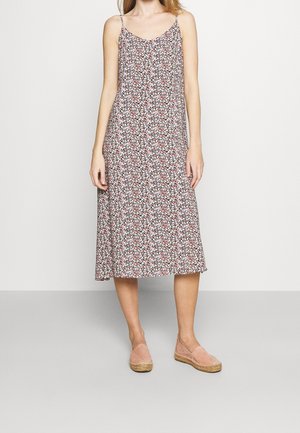 Femme portant une robe midi sans manches avec de fines bretelles et un petit motif floral, associée à des espadrilles roses.