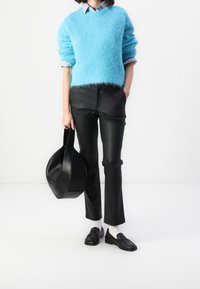 Pull bleu clair duveteux, pantalon en cuir noir, sac noir et mocassins. Chaussettes blanches visibles. Design épuré, moderne et structuré.