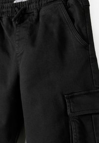 Pantalon cargo noir en coton avec une texture lisse, doté d'une taille à cordon de serrage, d'une poche sur le côté et de détails de poches à rabat.