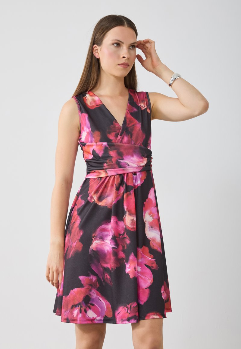 Robe florale noire avec des motifs abstraits roses et blancs, dotée d'un décolleté en V profond, d'un design sans manches et d'une taille ajustée menant à une jupe évasée.