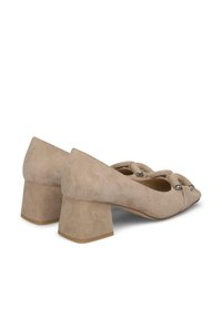 Chaussures à talons bloc en suède beige avec des pointes aigües, présentant un nœud décoratif et des accents métalliques à l'avant.