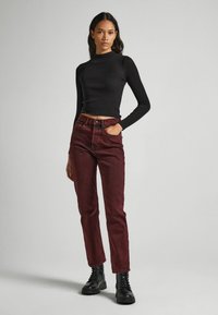 Fekete, hosszú ujjú crop top magas derekú bordó farmernadrággal és fekete fűzős csizmával párosítva, amely egy karcsú, testhezálló sziluettet mutat.